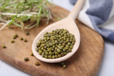 Photo of Wooden spoon with mung beans and board on table, closeup