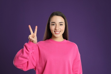 Woman showing number two with her hand on purple background