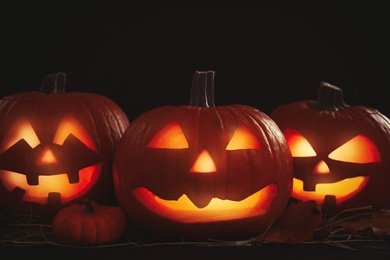 Photo of Glowing jack o'lanterns on table in darkness. Halloween decor