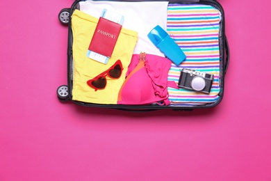 Photo of Open suitcase with beach objects on pink background, top view