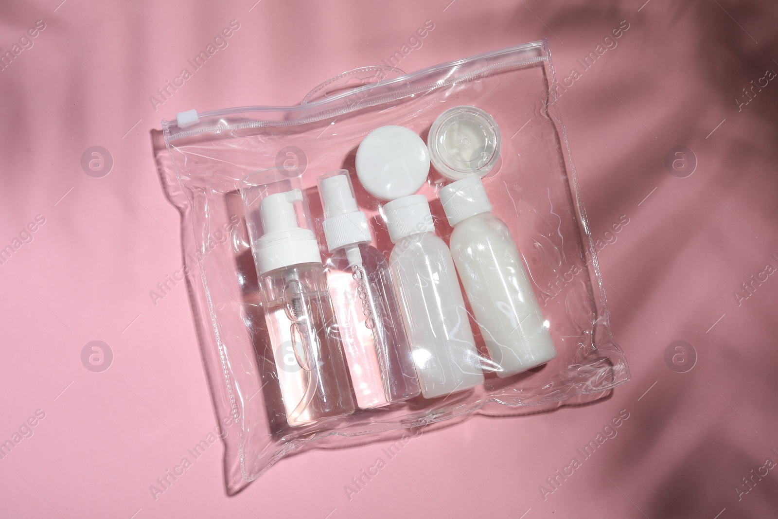 Photo of Cosmetic travel kit in plastic bag on pink background, top view. Bath accessories