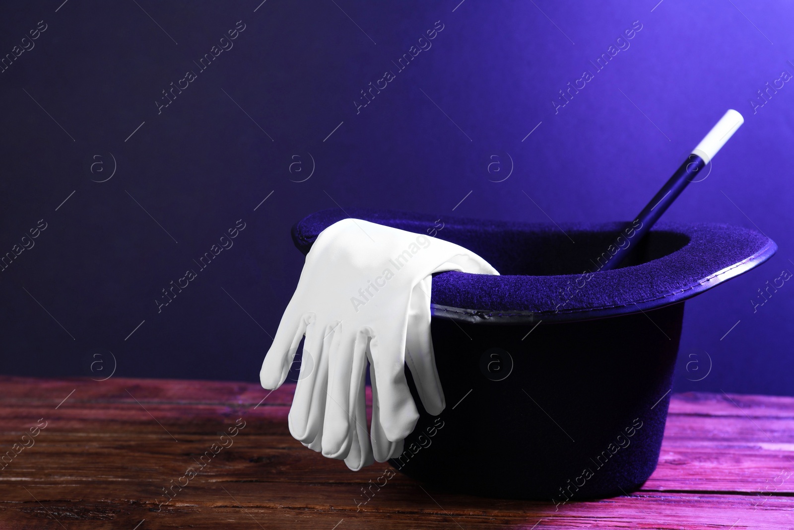 Photo of Top hat, gloves and wand on wooden table, space for text. Magician equipment