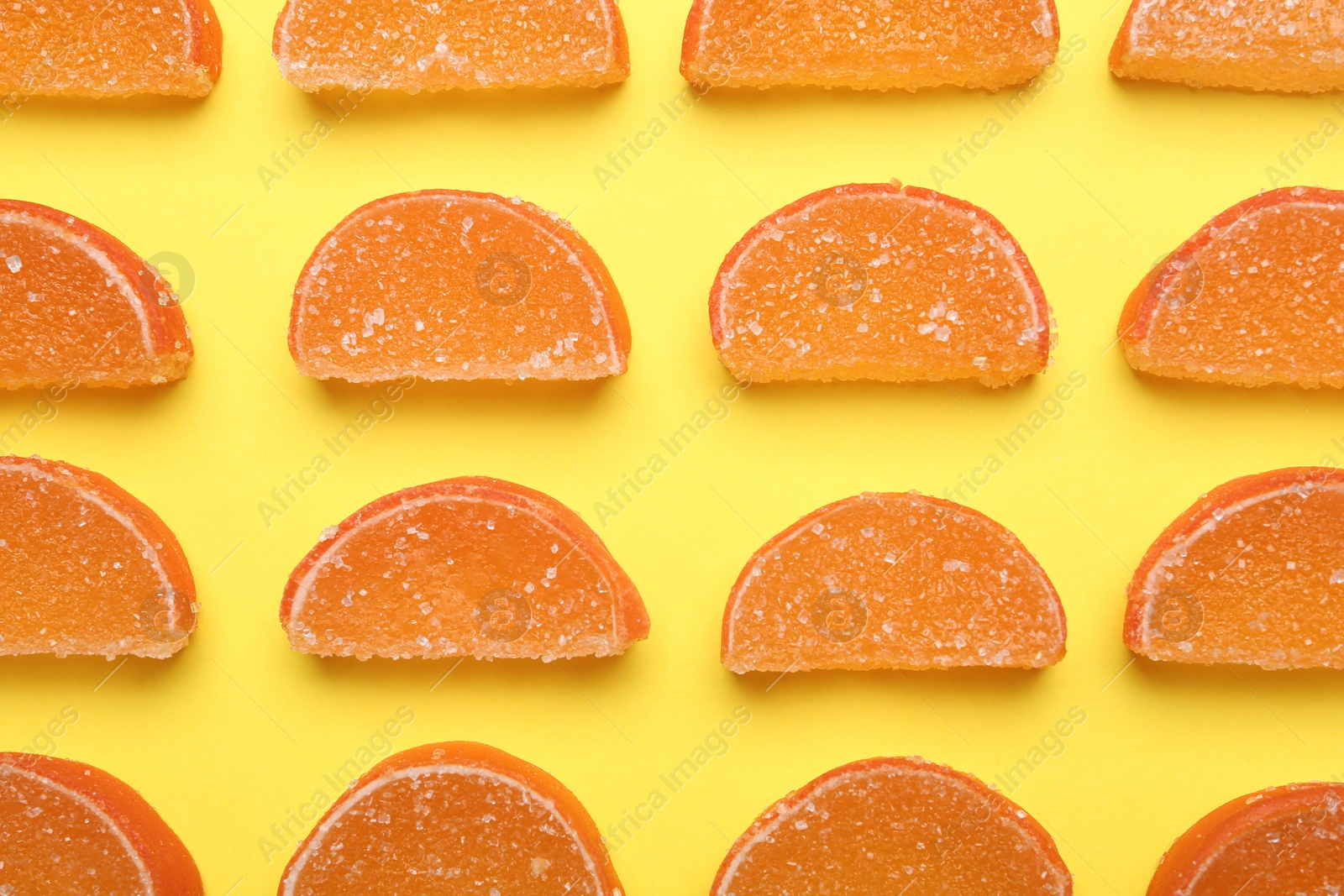 Photo of Delicious orange marmalade candies on yellow background, flat lay