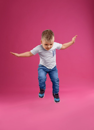 Photo of Cute little boy jumping on pink background