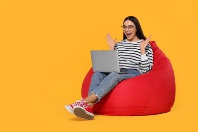 Photo of Excited woman with laptop sitting on beanbag chair against orange background