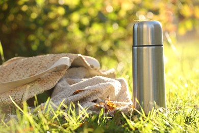 Photo of Metal thermos and bag with blanket on green grass outdoors