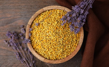 Photo of Fresh bee pollen granules in bowl and lavender on wooden table, top view