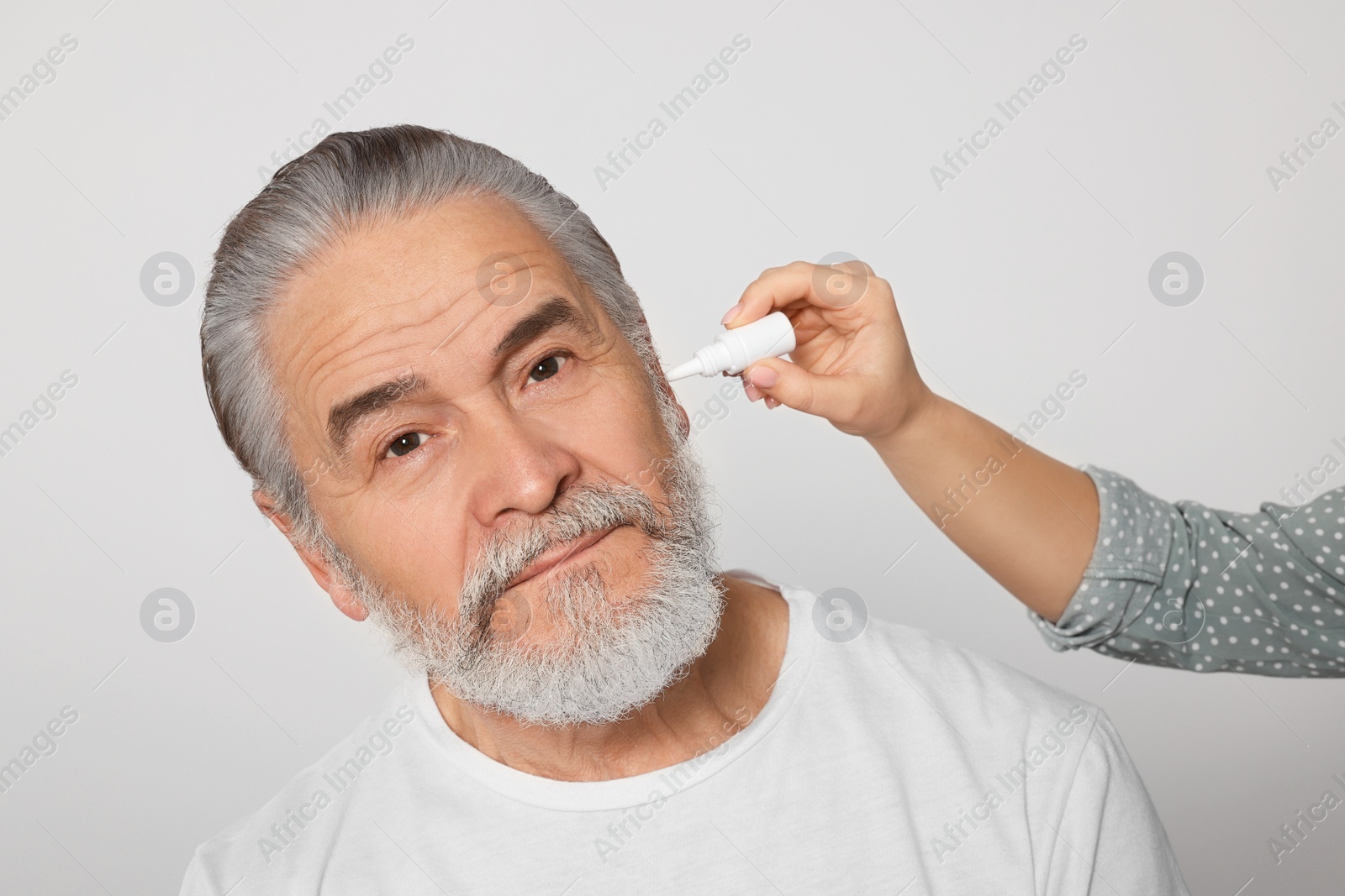 Photo of Young woman dripping medication into man's ear on white background