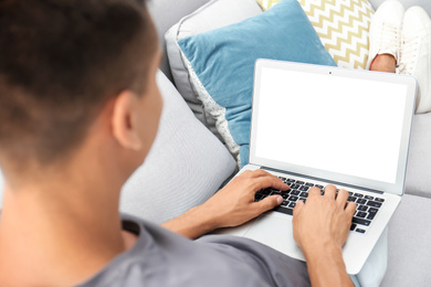 Young man using modern computer on sofa at home. Space for design