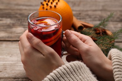 Photo of Woman with glass cup of aromatic mulled wine at wooden table, closeup