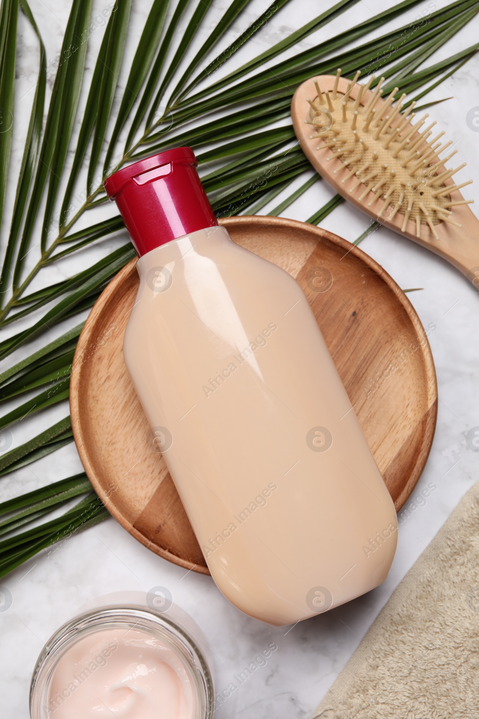 Photo of Bottle of shampoo, cream and hairbrush on white marble table, flat lay