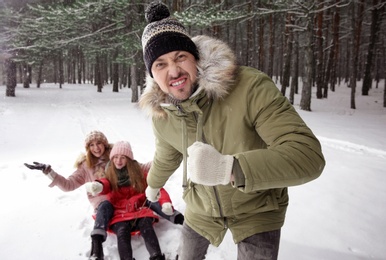 Photo of Father pulling sledge with his family in forest on snow day
