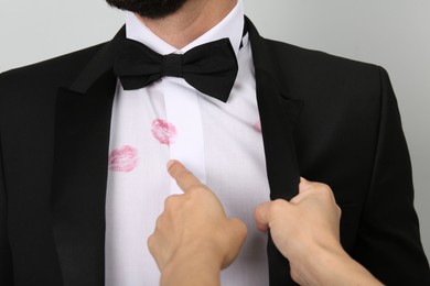 Photo of Woman pointing at lipstick kiss marks on her husband's shirt against white background, closeup
