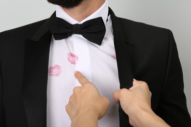 Woman pointing at lipstick kiss marks on her husband's shirt against white background, closeup