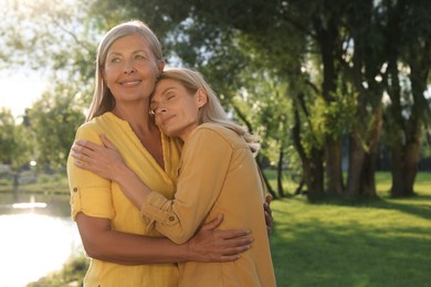 Family portrait of happy mother and daughter hugging in park on sunny day. Space for text