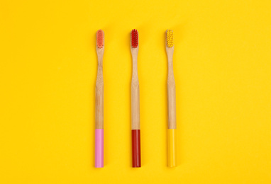 Photo of Toothbrushes made of bamboo on yellow background, flat lay. Space for text