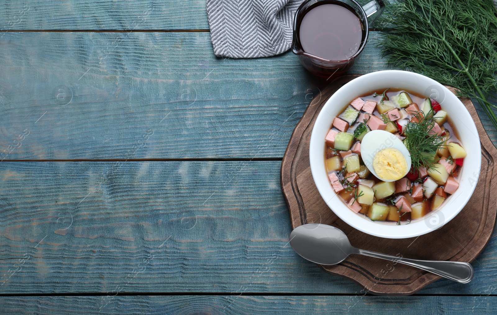 Photo of Delicious cold okroshka with kvass served on blue wooden table, flat lay and space for text. Traditional Russian summer soup