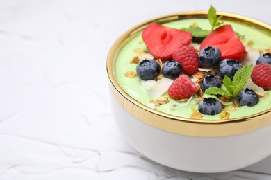 Photo of Tasty matcha smoothie bowl served with berries and oatmeal on white textured table, closeup with space for text. Healthy breakfast