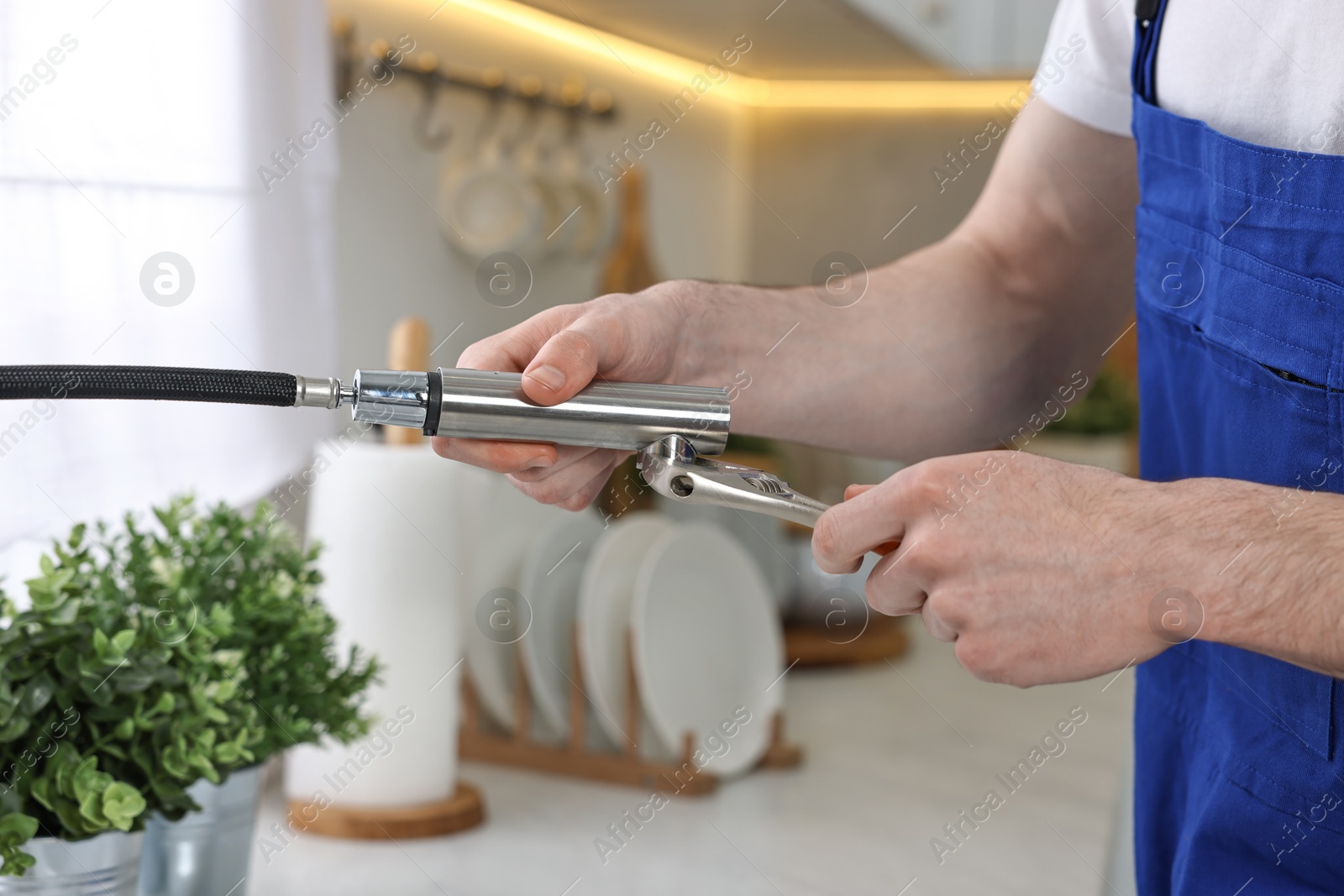 Photo of Plumber repairing faucet with spanner in kitchen, closeup