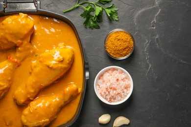Photo of Tasty chicken curry and ingredients on black textured table, flat lay. Space for text