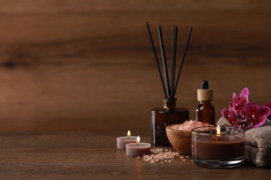 Beautiful spa composition with burning candles, sea salt and flowers on wooden table. Space for text