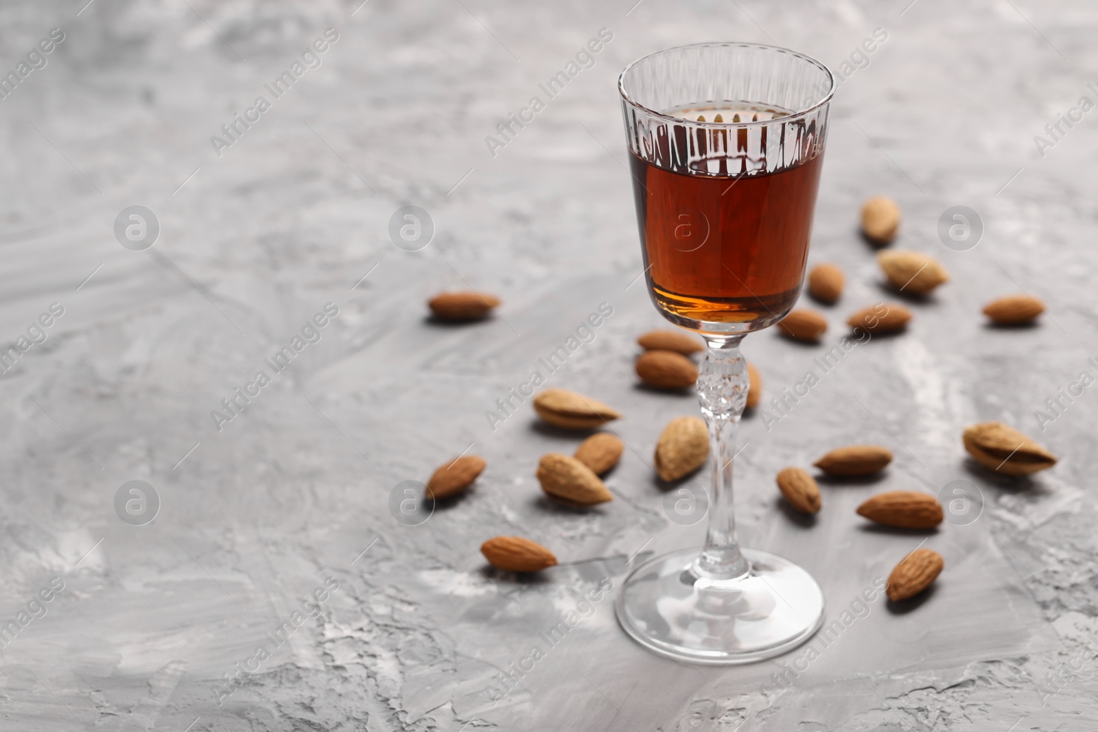 Photo of Liqueur glass with tasty amaretto and almonds on light grey table, closeup. Space for text