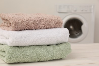 Photo of Stack of clean terry towels on white wooden table in laundry room