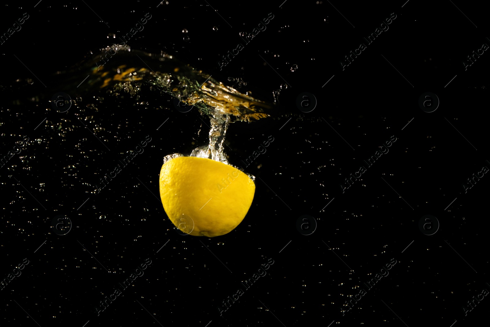 Photo of Lemon half falling down into clear water against black background