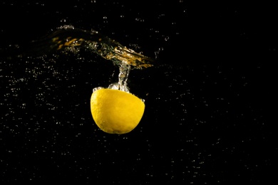 Photo of Lemon half falling down into clear water against black background