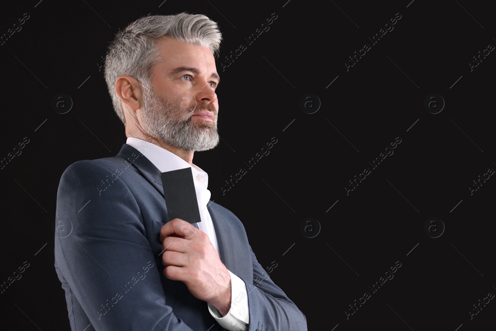 Photo of Handsome businessman holding blank business card on black background. Space for text