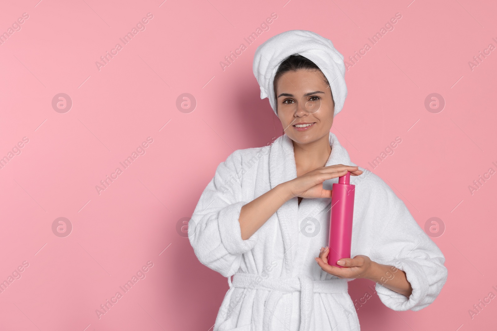 Photo of Beautiful young woman holding bottle of shampoo on pink background, space for text