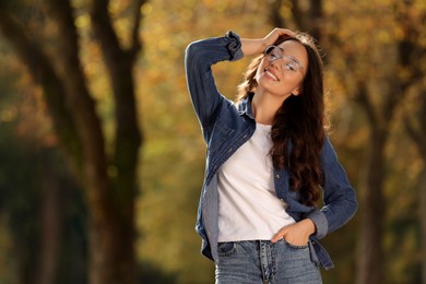 Young woman wearing eyeglasses in autumn park, space for text