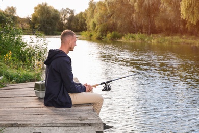 Man fishing on wooden pier at riverside. Recreational activity