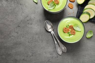 Photo of Tasty homemade zucchini cream soup served on grey table, flat lay. Space for text