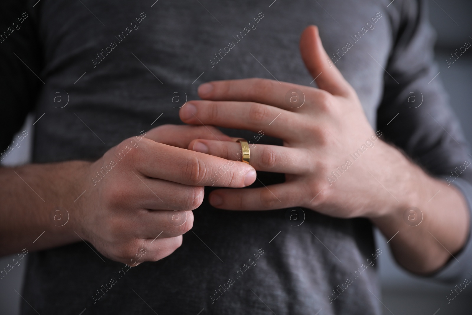 Photo of Man taking off wedding ring on blurred background, closeup. Divorce concept