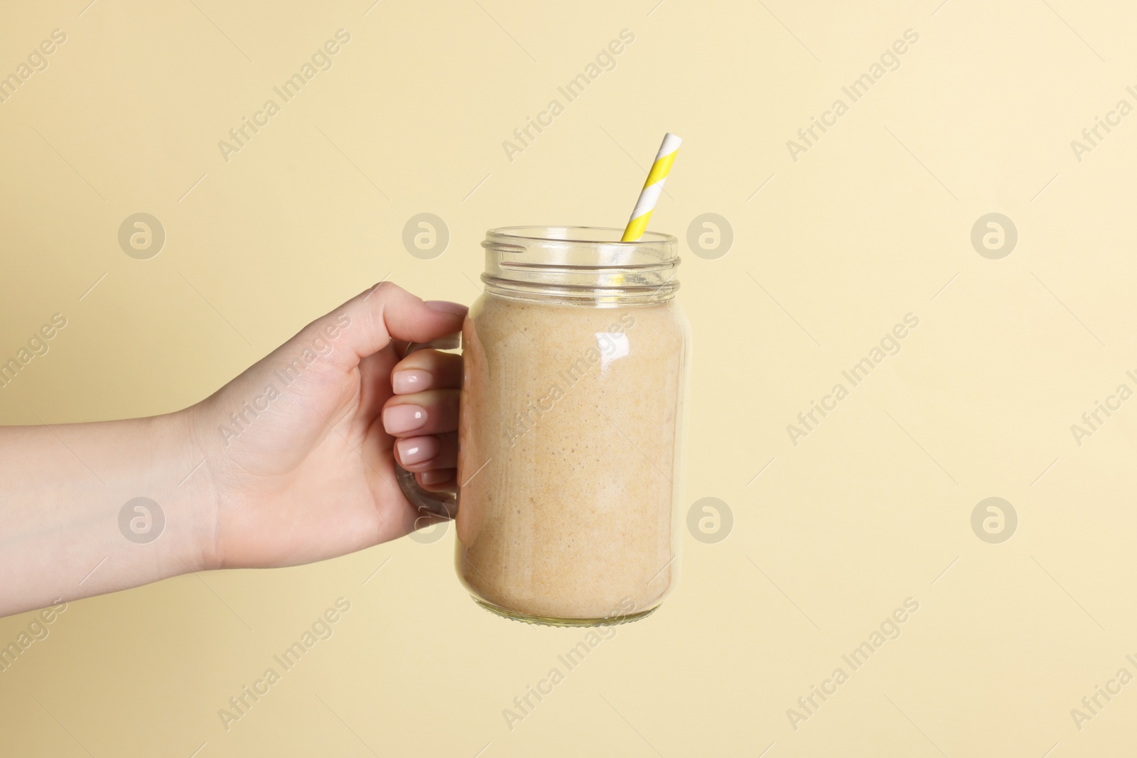 Photo of Woman holding mason jar of tasty smoothie on yellow background, closeup