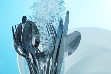 Washing silver cutlery and plates in water on light blue background