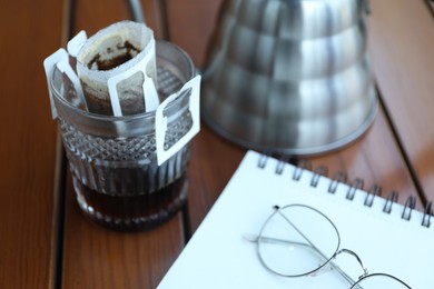 Photo of Glass with drip coffee bag on wooden table, closeup