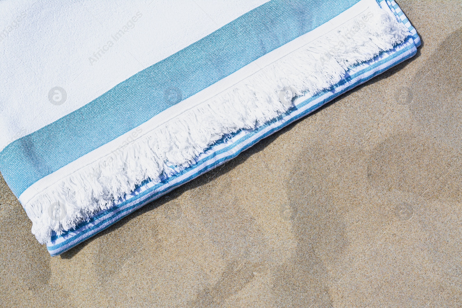 Photo of White and light blue striped towel on sandy beach, top view. Space for text