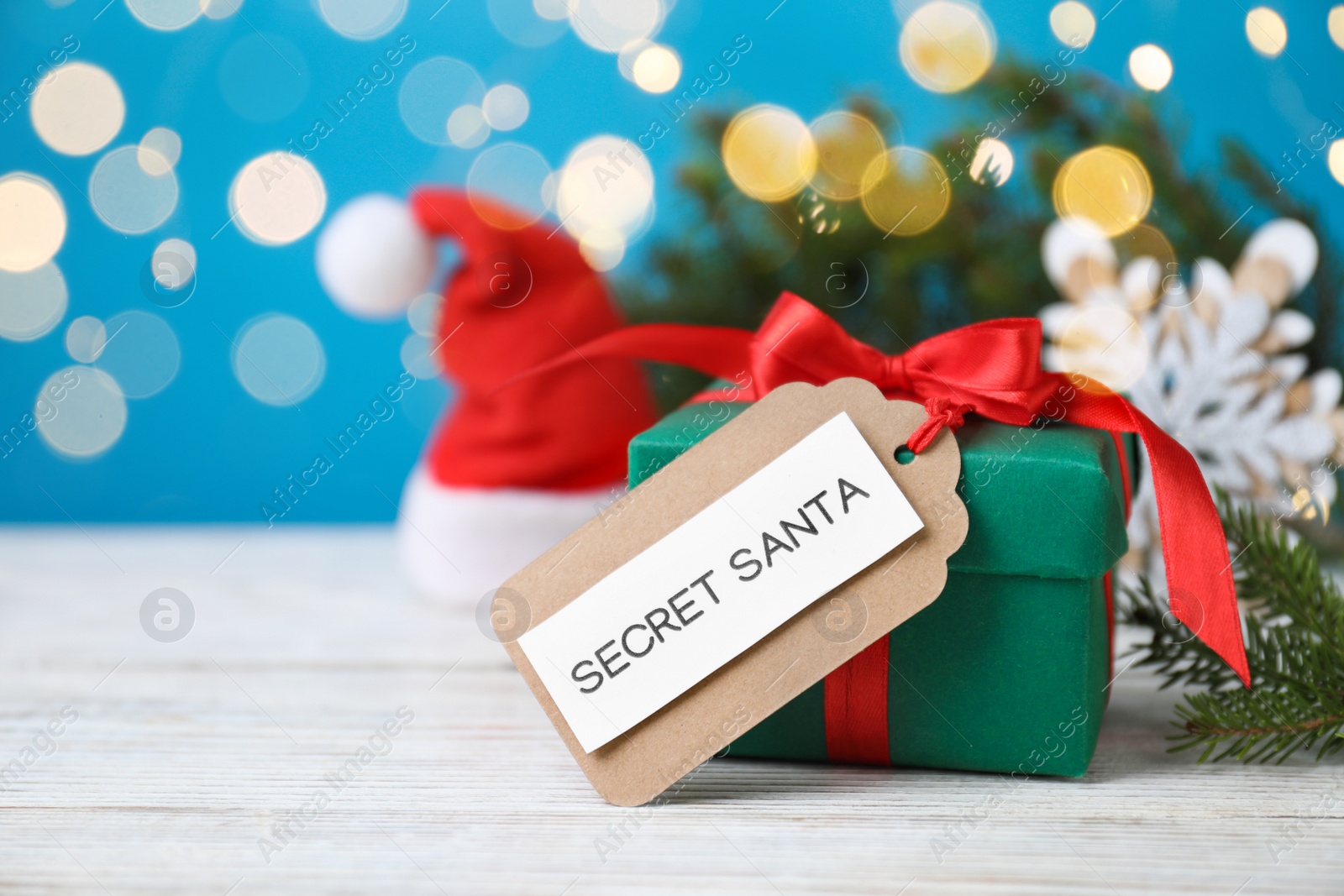 Photo of Present from secret Santa on white wooden table against blurred lights, space for text