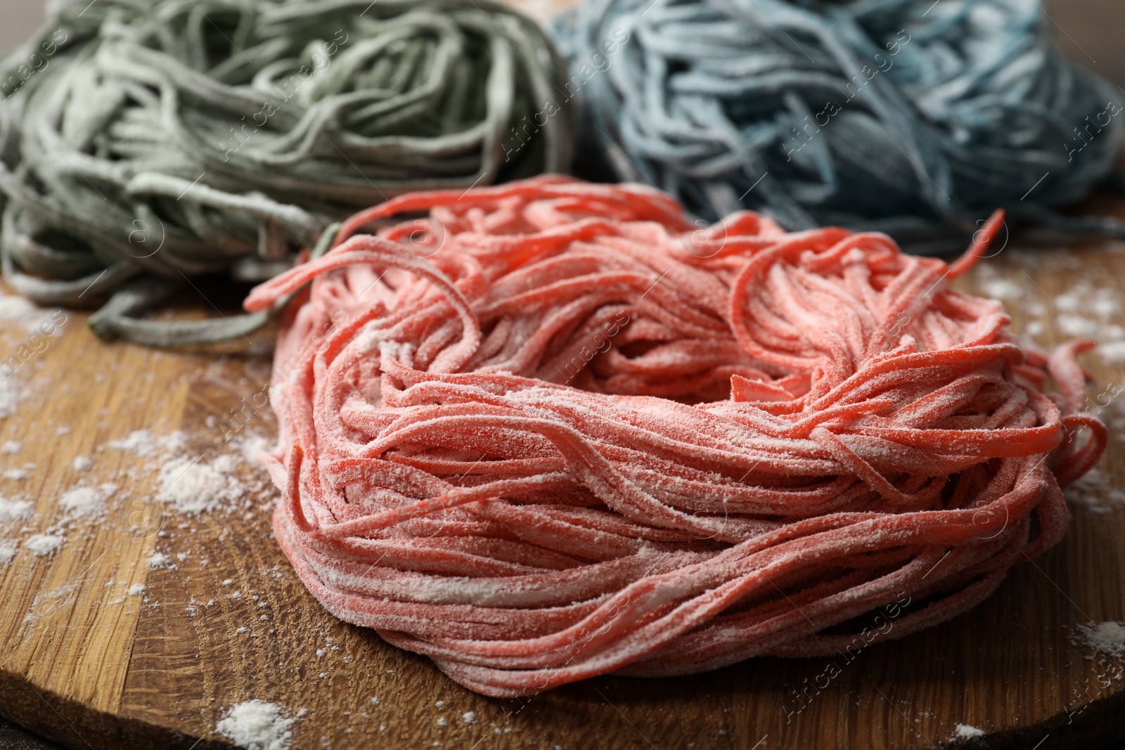 Photo of Rolled pasta painted with food colorings and flour on wooden table, closeup