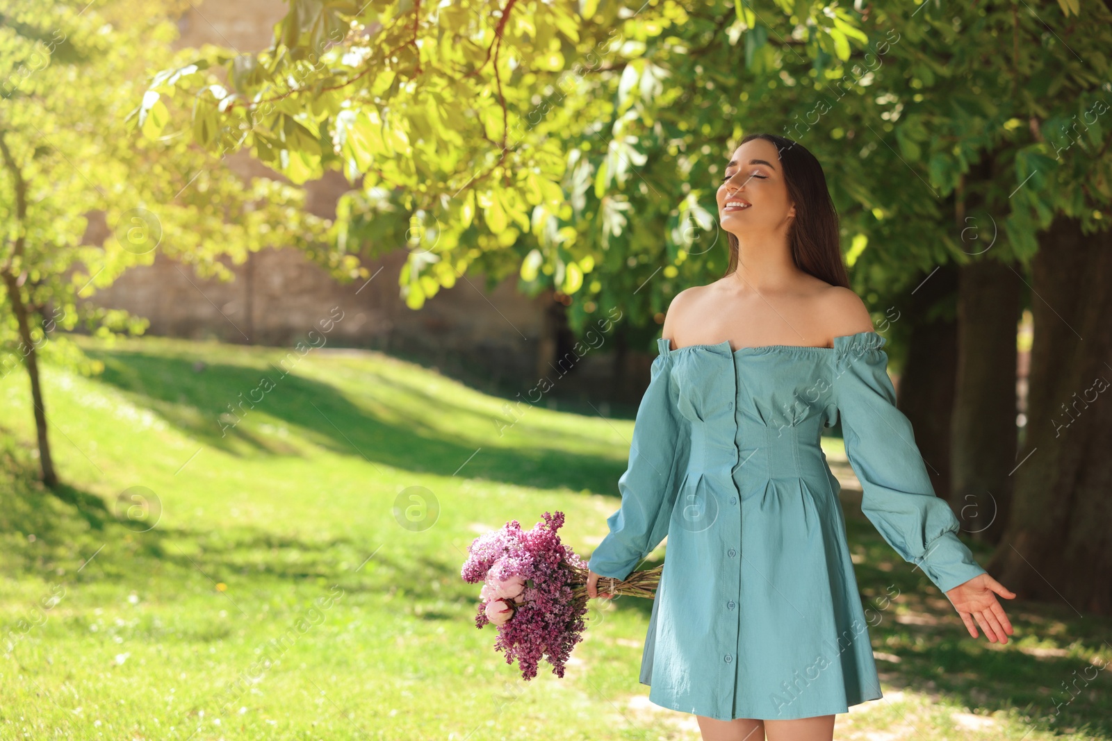 Photo of Beautiful woman with bouquet of spring flowers in park on sunny day, space for text