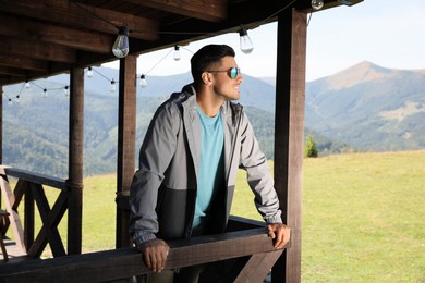 Handsome man enjoying beautiful mountain landscape on wooden terrace