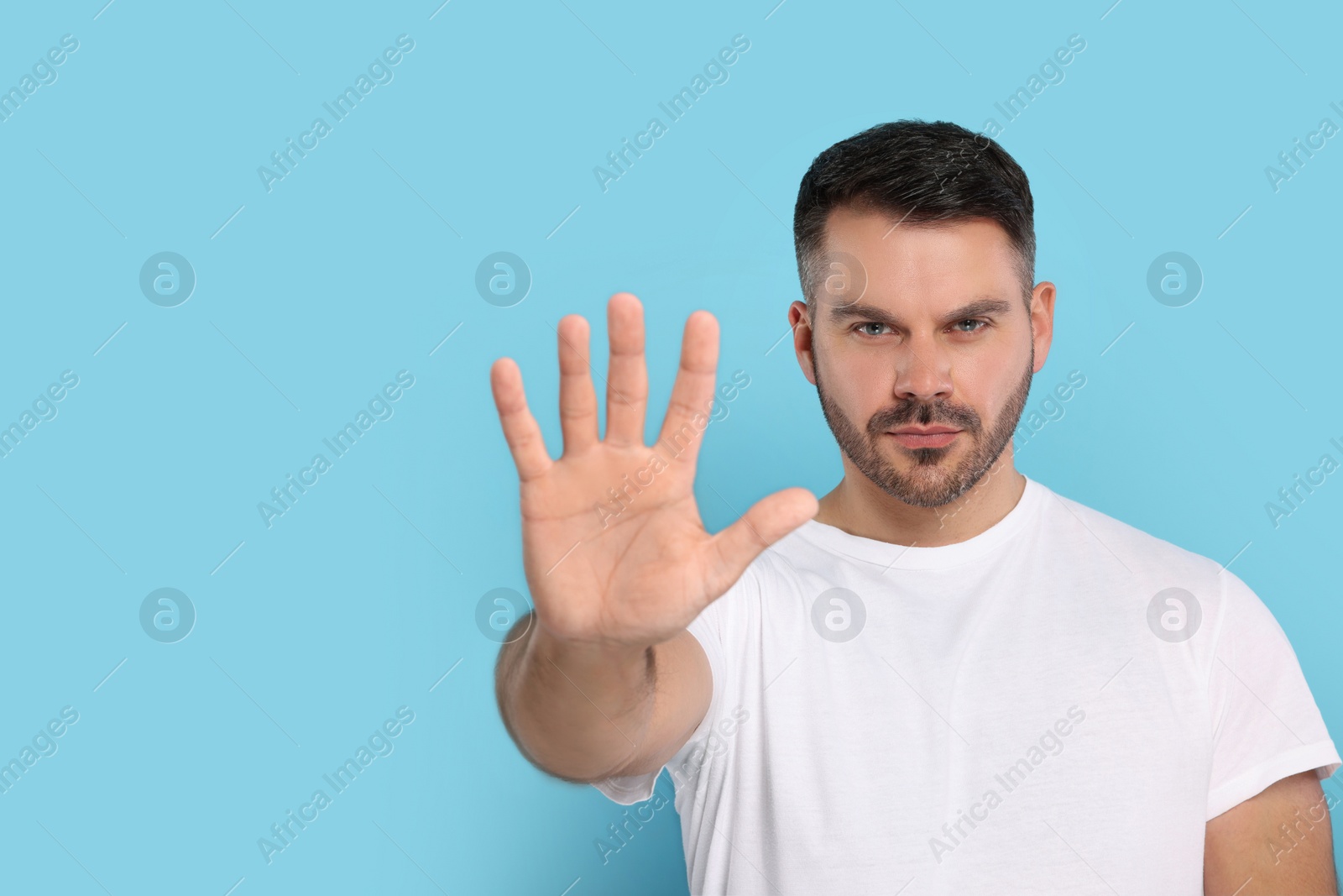 Photo of Handsome man showing stop gesture on light blue background, space for text