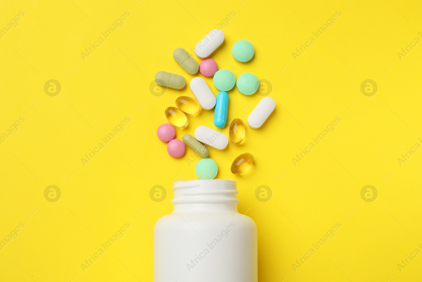 Photo of Different vitamin pills and bottle on yellow background, top view.