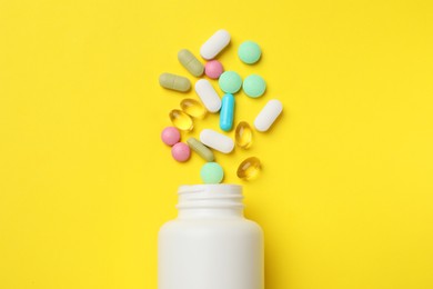 Photo of Different vitamin pills and bottle on yellow background, top view.