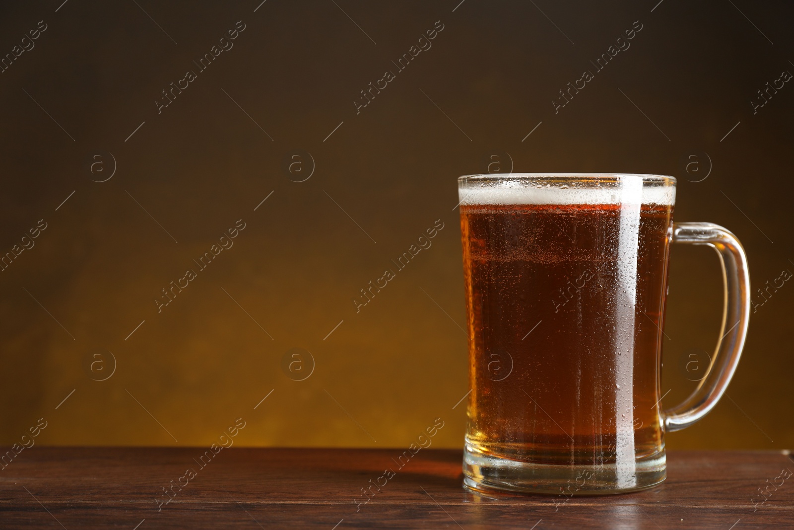 Photo of Mug with fresh beer on wooden table against dark background. Space for text