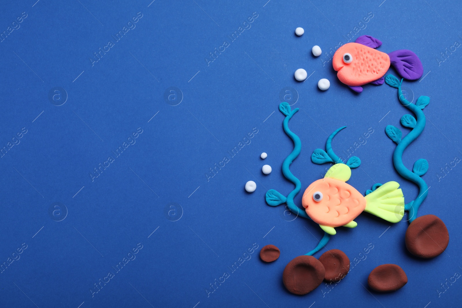 Photo of Colorful fish, water plants and stones made with play dough on blue background, flat lay. Space for text