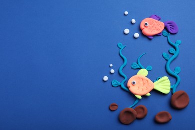 Photo of Colorful fish, water plants and stones made with play dough on blue background, flat lay. Space for text