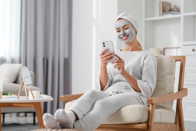 Photo of Young woman with face mask using smartphone at home. Spa treatments